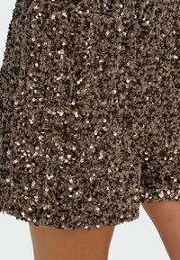 Hnědé šortky se šupinkami, které se vyznačují hustě zdobeným vzorem lesklých kulatých šupinek, se zelenou měkkou texturou a uvolněným střihem.