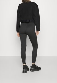 Svart kort sweatshirt med långa ärmar, tillsammans med åtsittande svarta tights och svarta sportskor med reflektande detaljer.