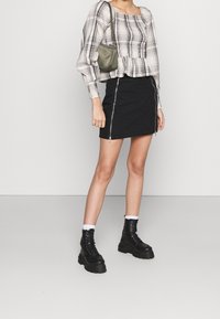 Gonna in denim nero con cerniere laterali, abbinata a una maglietta a palloncino a quadri. Presenta stivali neri tipo combat e una borsa a spalla verde.