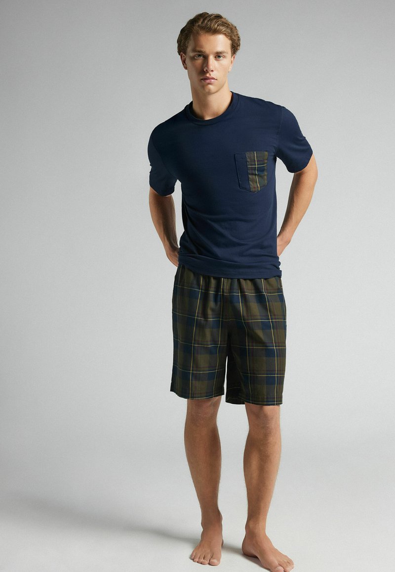 Marineblå bomulls t-shirt med en rutigt ficka, kombinerad med grön och marinblå rutiga shorts. Outfiten har en elastisk midja och en avslappnad passform.