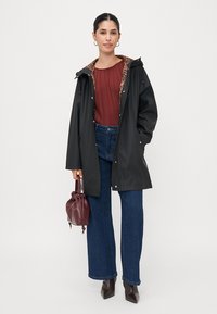 Giacca nera impermeabile con fodera a stampa leopardata, abbinata a una blusa plissettata color ruggine, jeans larghi blu e una borsa bordeaux.
