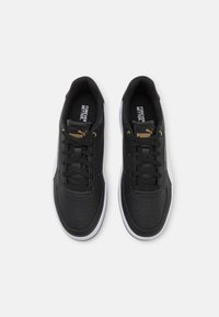 Black sneakers with a smooth leather upper, perforated toe box, black laces, a white rubber sole, and gold brand logo accents.