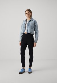 Cropped light blue denim jacket, white top, black leggings, and blue sneakers. Features two pockets on the jacket. Smooth texture throughout.