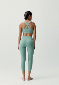 Mentolovo zelený športový podprsenka s prekríženými popruhmi na chrbte, v kombinácii s vysokými legínami, ktoré sú vyrobené z hladkej, elastickej tkaniny.