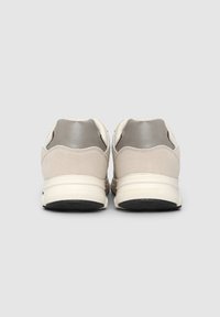 Scarpe da ginnastica beige con accenti grigi, caratterizzate da una tomaia in camoscio, un tallone testurizzato e una suola ammortizzata. La vista posteriore mostra i dettagli del sistema di allacciatura.