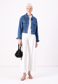 Denim jakna v temno modri barvi, bela majica, široke bele hlače, nagi sandali, drži majhno črno cvetlično torbico.