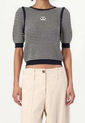 Maglione a righe navy e crema con maniche a puff corte, polsini a costine e un dettaglio logo argentato sul petto. Abbinato a pantaloni beige.