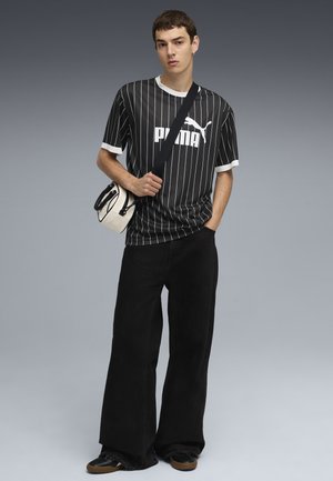 Black and white striped short-sleeve jersey featuring a bold "PUMA" logo, paired with wide black denim pants and a small crossbody bag.