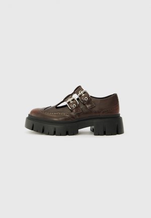 Sapatos de couro castanho com design recortado, duplo fecho prateado, sola grossa preta e detalhes de brogue ao longo das bordas.