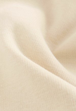 Hellbeiger Stoff mit feinem, strukturierten Strickmuster; weiche, glatte Oberfläche, die sanft fällt und die Dehnbarkeit betont.