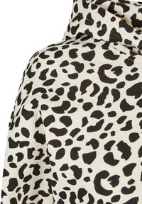 Tissu blanc avec motif léopard noir irrégulier et coutures visibles sur un vêtement à capuche.