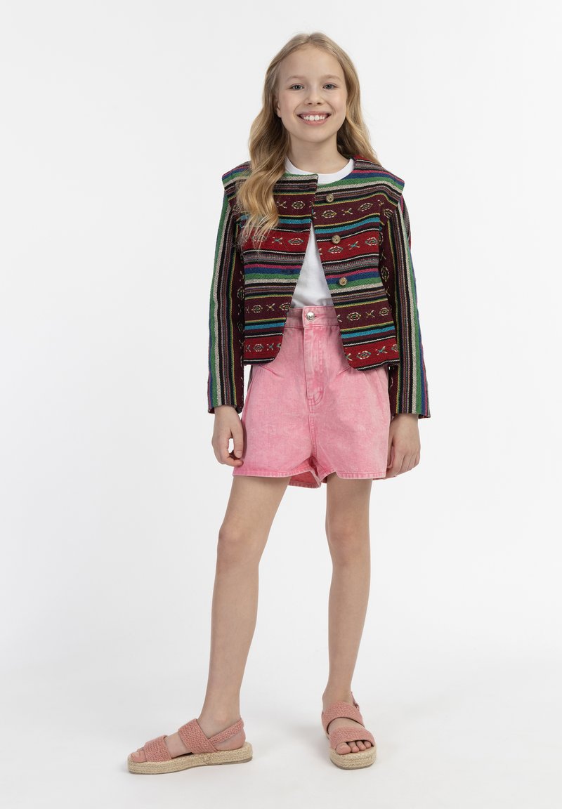 Spalvota austinė striukė su vertikaliomis juostelėmis, derinama su šviesiai rožiniais džinsiniais šortais ir rožiniais pintais sandalais. Pasiūtas paprastas baltas marškinėliai po juo.