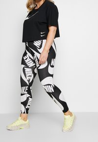 Svart kortärmad t-shirt med vit Nike-logotyp, i kombination med svarta tights som har stor vit Nike-branding och detaljer. Inkluderar gula sneakers.