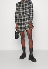 Svart- och vitrutigt klänning med långa ärmar, knappstängning, flerlagers volangsläpp, parat med svarta ankelstövlar och en liten handväska.