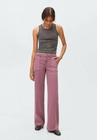 Top gris de tirantes acanalados y pantalones rosas de talle alto y perneras anchas con bolsillos frontales. La modelo lleva un collar con un colgante de flor y zapatos oscuros.