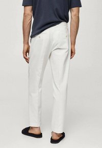 Białe lniane spodnie o prostym kroju, z dwoma tylnymi kieszeniami i subtelną teksturą, w połączeniu z czarnymi klapkami.