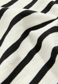Tissu rayé noir et blanc présentant des rayures audacieuses alternées sur une surface texturée et tricotée, démontrant douceur et élasticité.