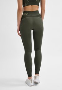 Olivgröna ribbade leggings med hög midja, kontrasterande sömmar och en åtsittande design, kombinerat med vita träningsskor.