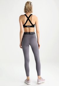 Sort sports-bh med krydsrygdesign, grå leggings med en sort talje, der har "PRO NIKE" tekst, og lyserøde træningssko.