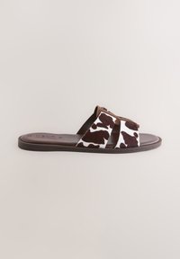 Cow-Print Slide-Sandale mit weichem, strukturiertem Obermaterial und braunen Akzenten. Flache Sohle für bequemen Tragekomfort, geeignet für legere Umgebungen.
