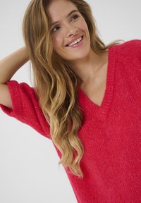 Pull rouge en tricot avec un décolleté en V, des manches courtes et une finition texturée. Coupe douce et ample avec un design décontracté.