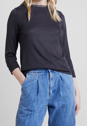 Dunkelgraues Langarmoberteil mit strukturiertem Ausschnitt, kombiniert mit hoch taillierten, faltigen blauen Jeanshosen mit heller Waschung.