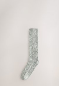 Chaussette grise en tricot avec un bord côtelé, présentant un mélange texturé pour la chaleur et le confort. La chaussette s'étend jusqu'au milieu du mollet.