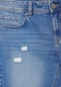 Niebieskie dżinsy z małymi przetarciami w pobliżu przedniej kieszeni oraz widocznymi pomarańczowymi przeszyciami.