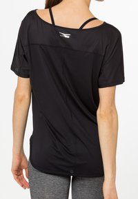 Camiseta deportiva negra de corte holgado, mangas cortas y cuello redondo. Presenta un logo en la parte superior de la espalda y un tejido texturizado.