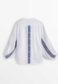 Witte linnen blouse met lange, luchtige mouwen, voorzien van een blauw geometrisch borduurpatroon langs de middenrug en de randen van de mouwen.
