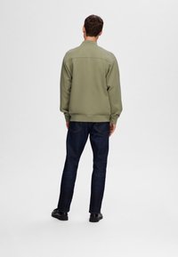 Sweatshirt vert avec un col haut, texture douce et ourlet côtelé, associé à un jean en denim bleu foncé et des chaussures noires.