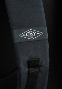 Cinghia in tessuto nero con motivo testurizzato, dotata di una toppa rettangolare con l'etichetta "DRY GOODS CO" in bianco su uno sfondo scuro.