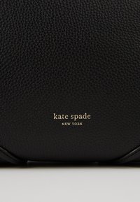 Sort læderhåndtaske med en struktureret finish og "kate spade NEW YORK" præget i guld på forsiden.