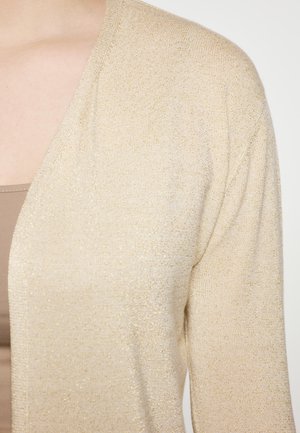 Beige, kevyt neulejakku, jossa on huomaamaton kiilto, avoin etuosa, tekstuurinen neulekangas ja pudotetut olkasaumat.