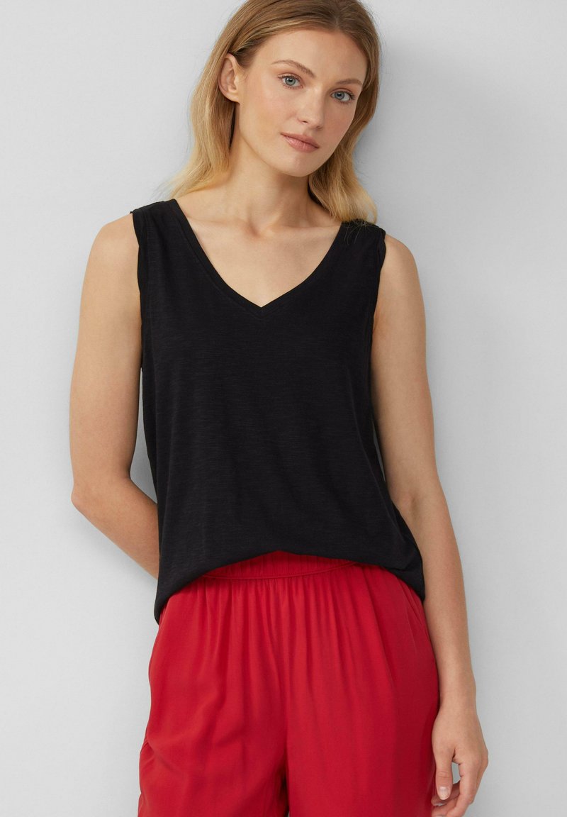 Top nero senza maniche con scollatura a V, vestibilità comoda e texture morbida, abbinato a pantaloni rossi con vita elastica. Sfondo neutro.