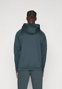 Bluza z kapturem w ciemnym odcieniu teal, wykonana z gładkiego, teksturowanego materiału. Charakteryzuje się luźnym krojem, rękawami raglanowymi oraz ściągaczem u dołu.