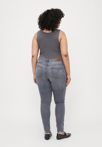 Gray bodysuit with a rounded neckline paired with gray skinny jeans featuring a brown leather patch and a frayed hem. Black studded flats.