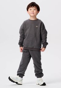 Grijze sweatshirt met ribgebreide manchetten en onderkant, voorzien van een klein logo. Gekocht met bijpassende joggingbroek en witte sportschoenen.