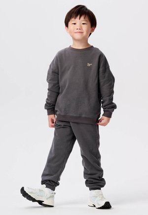 Grijze sweatshirt met ribgebreide manchetten en onderkant, voorzien van een klein logo. Gekocht met bijpassende joggingbroek en witte sportschoenen.