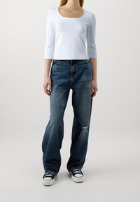 Top azzurro chiaro a maniche lunghe con scollatura quadrata abbinato a jeans a gamba larga blu scuro con dettagli strappati, indossato con sneakers nere.