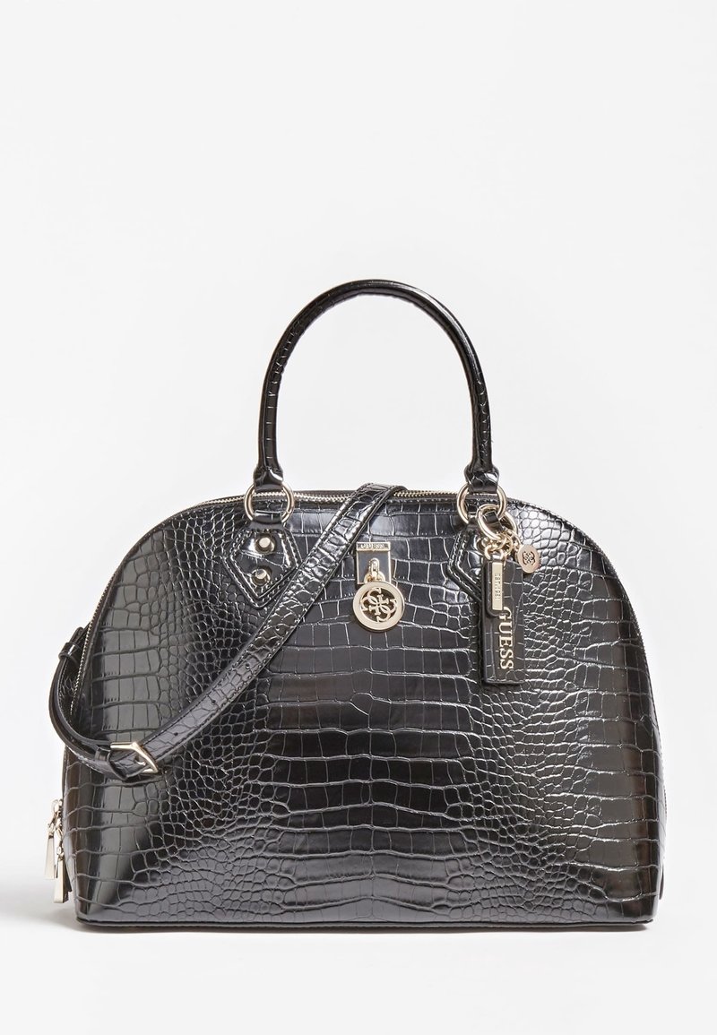 Sac à main en cuir synthétique noir effet crocodile avec double poignées, bandoulière amovible et pendentifs logo Guess dorés sur fond blanc.