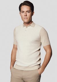 Beżowa koszulka polo z krótkim rękawem, o teksturowanym wzorze, z zapięciem na guziki i dopasowanym fasonie. Można zestawić z jasnymi chinosami.