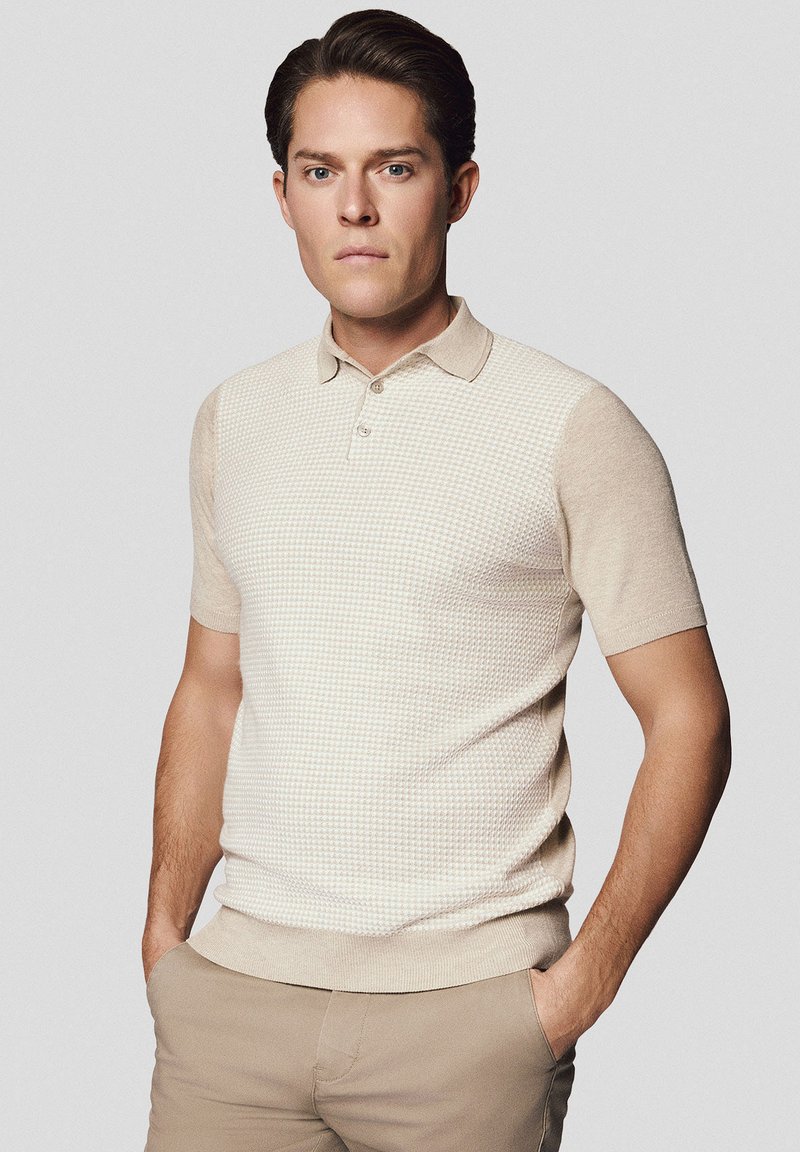 Beżowa koszulka polo z krótkim rękawem, o teksturowanym wzorze, z zapięciem na guziki i dopasowanym fasonie. Można zestawić z jasnymi chinosami.