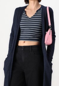 Námořnický dlouhý cardigan, pruhovaný námořnický a bílý crop top, černé džíny s vysokým pasem a malá růžová texturovaná kabelka se stříbrným akcentem.