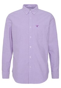Camicia a maniche lunghe di un leggero lavanda con colletto a bottoni, taschino anteriore e logo ricamato di un'aquila in viola scuro sul petto.