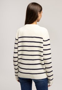 Biało-granatowy sweter w paski o ryflowanej fakturze, okrągłym dekolcie i długich rękawach. Tył ma poziome paski.