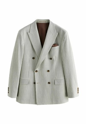Hände, die die Manschette eines beige gestreiften Blazers mit großen dunklen Knöpfen und einer Vordertasche anpassen.