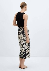 Top senza maniche nero abbinato a una gonna floreale nera e crema lunghezza ginocchio. Vestibilità aderente con tessuto morbido e sandali piatti semplici.