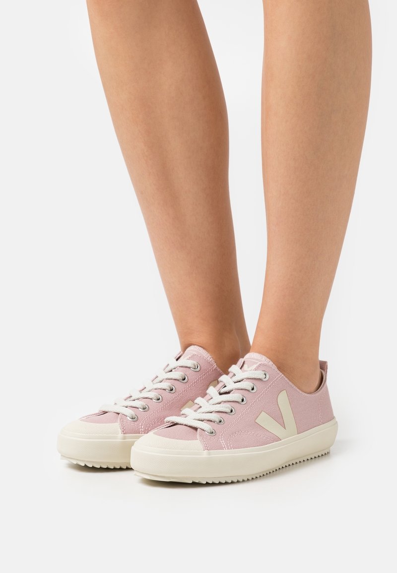 Baskets en toile rose clair avec semelles en caoutchouc blanches, présentant des accents et des lacets couleur crème, et un logo « V » sur chaque côté.