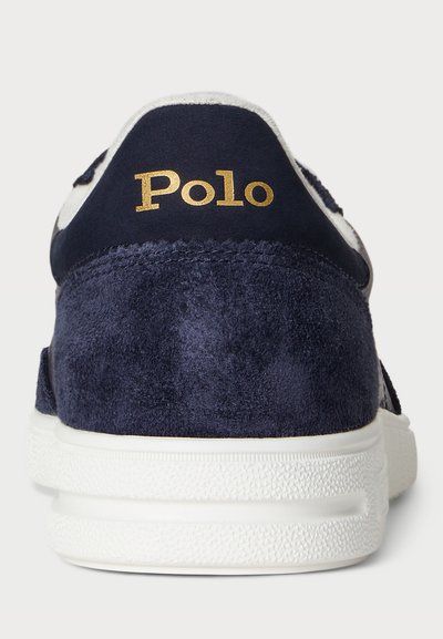 Marineblauwe suède sneaker met een witte rubberen zool, een gouden "Polo" logo op de hiel en een getextureerde achterkant voor extra grip.